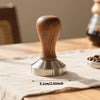 A precision espresso tamper set featuring a wooden handle and stainless steel base resting on a light linen cloth.