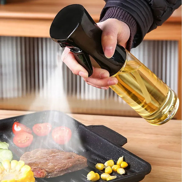 Eine Hand sprüht goldenes Öl aus einer dunklen Flasche auf Essen auf einer schwarzen Platte.