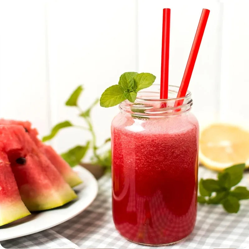 A glass jar filled with red juice and garnished with a mint leaf and two red straws.