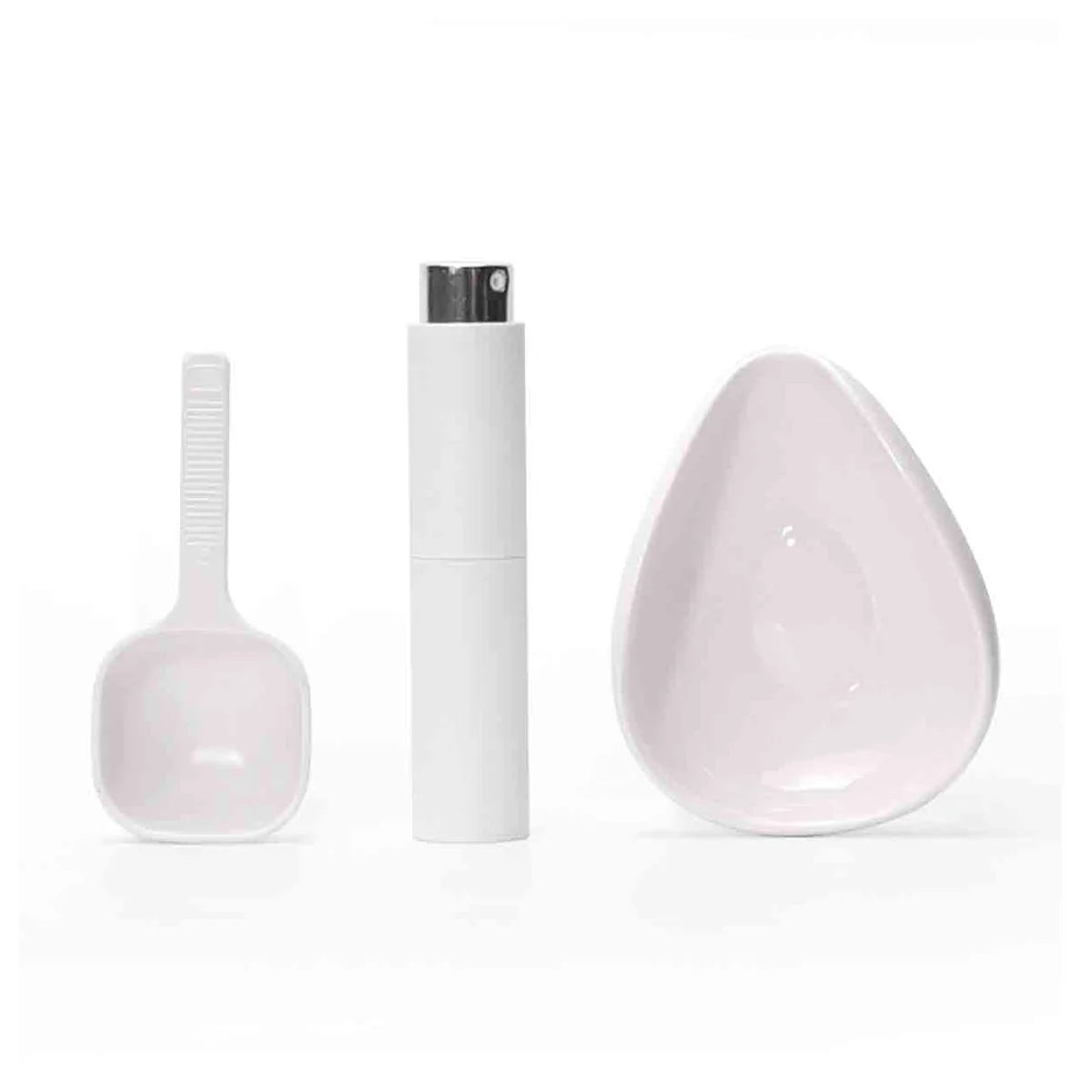 A white ceramic coffee dosing and spray kit showing a measuring spoon and a small dish.