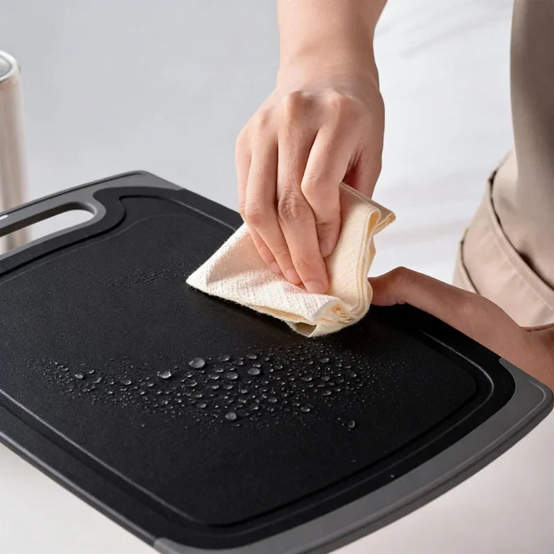 A hand is wiping a black silicone kitchen knife and tool set with a white cloth.