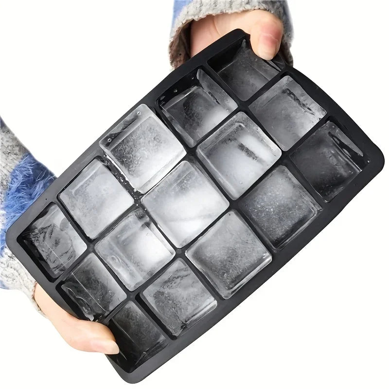 A hand holds a black silicone ice cube mold with diamond shapes filled with ice.