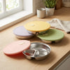 A set of stackable stainless steel divided dinner plates with colorful lids resting on a wooden surface.