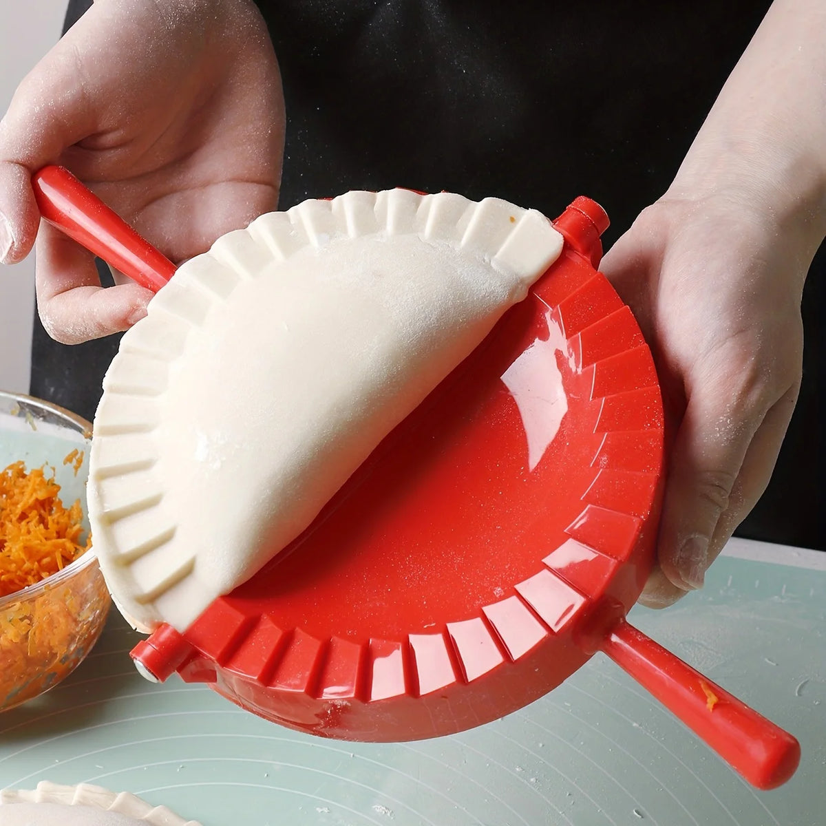 A hand is pressing dough into a red manual dumpling press for homemade pastries.
