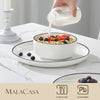 A hand pours a white liquid into a bowl of fruit and grains on a ceramic plate.