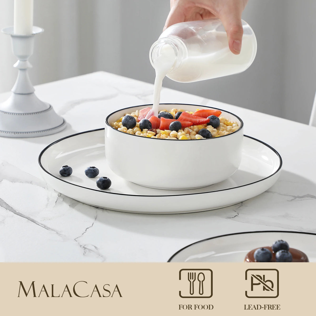 A hand pours a white liquid into a bowl of fruit and grains on a ceramic plate.