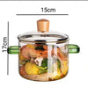A clear glass soup pot with a wooden lid filled with various ingredients like vegetables and seafood.