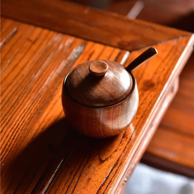 A vintage wooden salt and spice shaker set with a lid resting on a polished wooden surface.