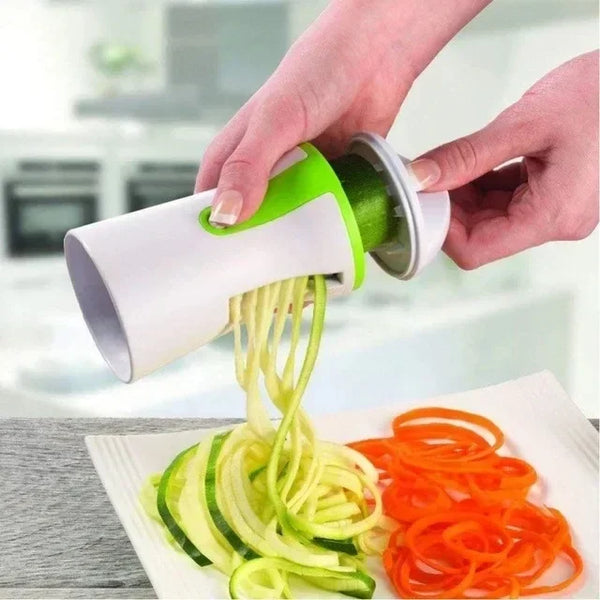 Eine Hand benutzt einen grünen Küchenspiralisierer, um aus Zucchini und Karotten dünne Nudeln zu machen.
