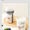 A double-layer container of overnight oats with fruit and nuts is shown next to a small bowl of berries.