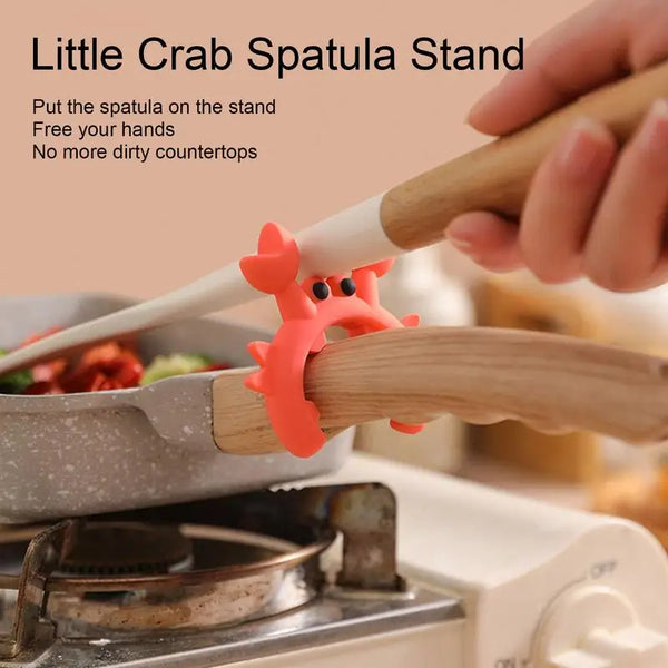 Eine Hand legt einen orangen krabbenförmigen Silikonspatel auf einen Holzständer zur Aufbewahrung.