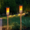 Two tall solar flame effect garden path lights with warm glowing bulbs standing in a green landscape.
