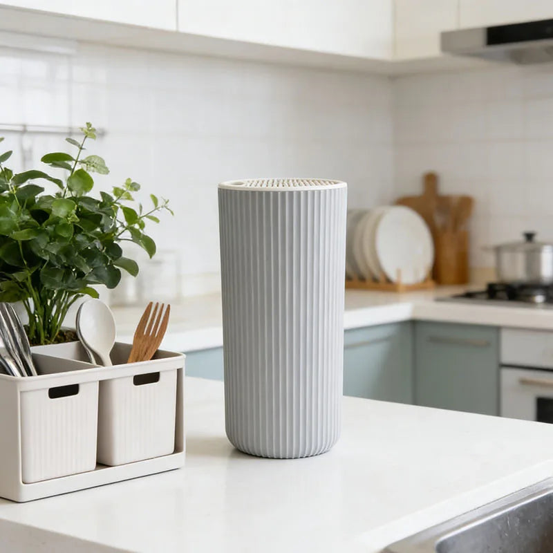 A tall, ribbed gray organizer for knives sits on a white countertop in a bright kitchen setting.