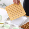 A hand is placing a wooden tea infuser into a white ceramic tray with small green bowls.