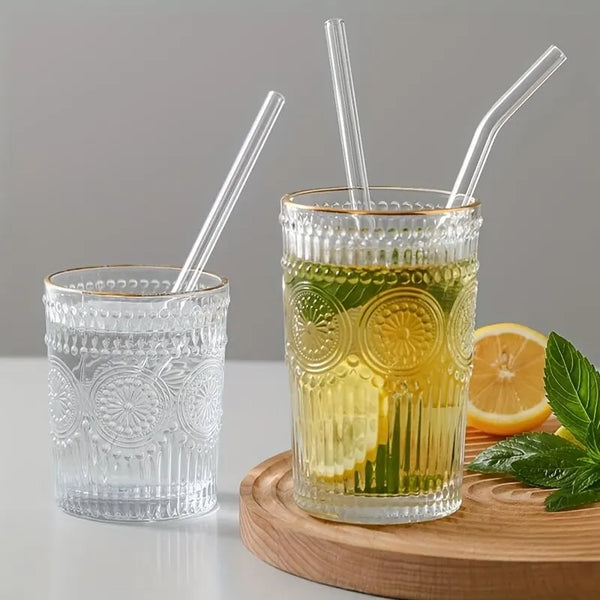 Ein Glas mit gelbem Getränk und drei klare Strohhalme auf einer Holzunterlage.