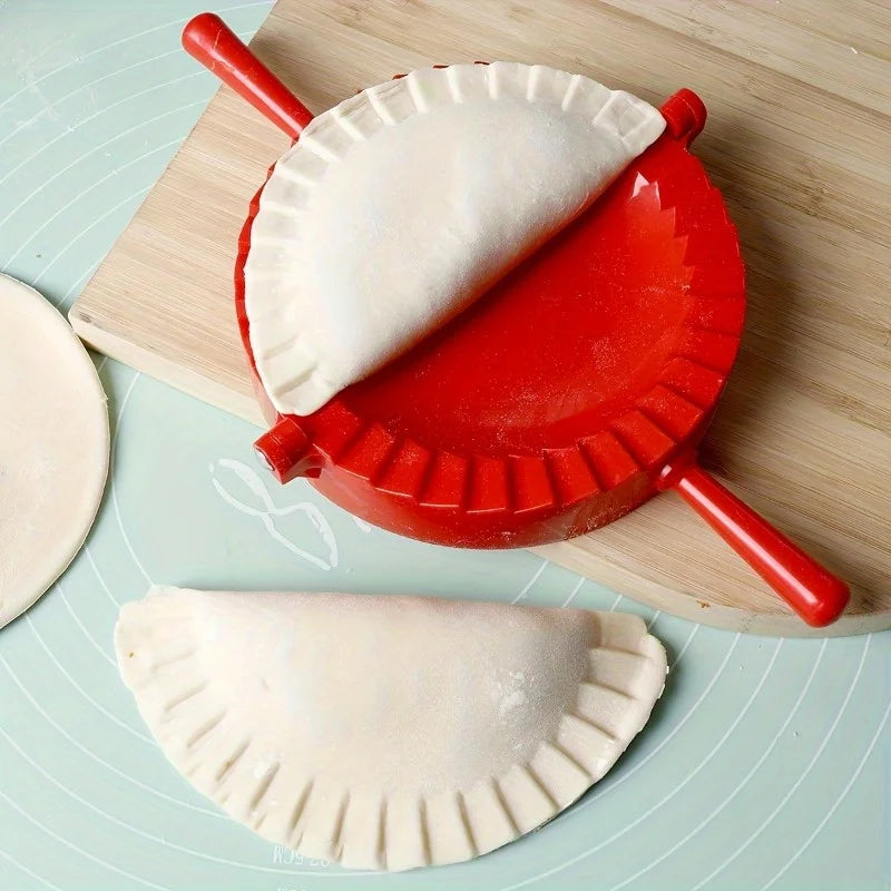 A red manual dumpling press is shown on a wooden board with two white pastry wrappers.