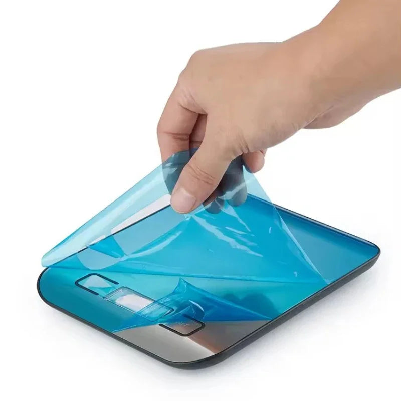 A hand is holding a transparent blue digital kitchen scale with a silver base.