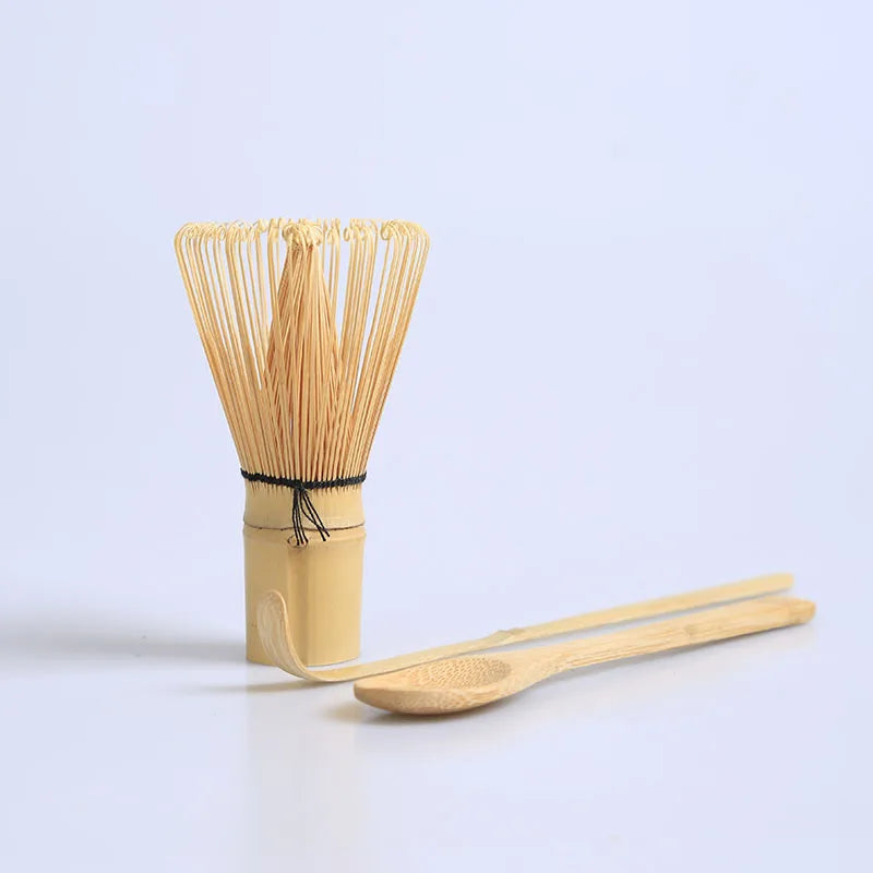 A traditional bamboo and ceramic matcha tea set featuring a bundle of bamboo whisks and a wooden scoop.