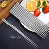 A set of stainless steel chopsticks resting on a wooden board next to citrus fruit and strawberries.
