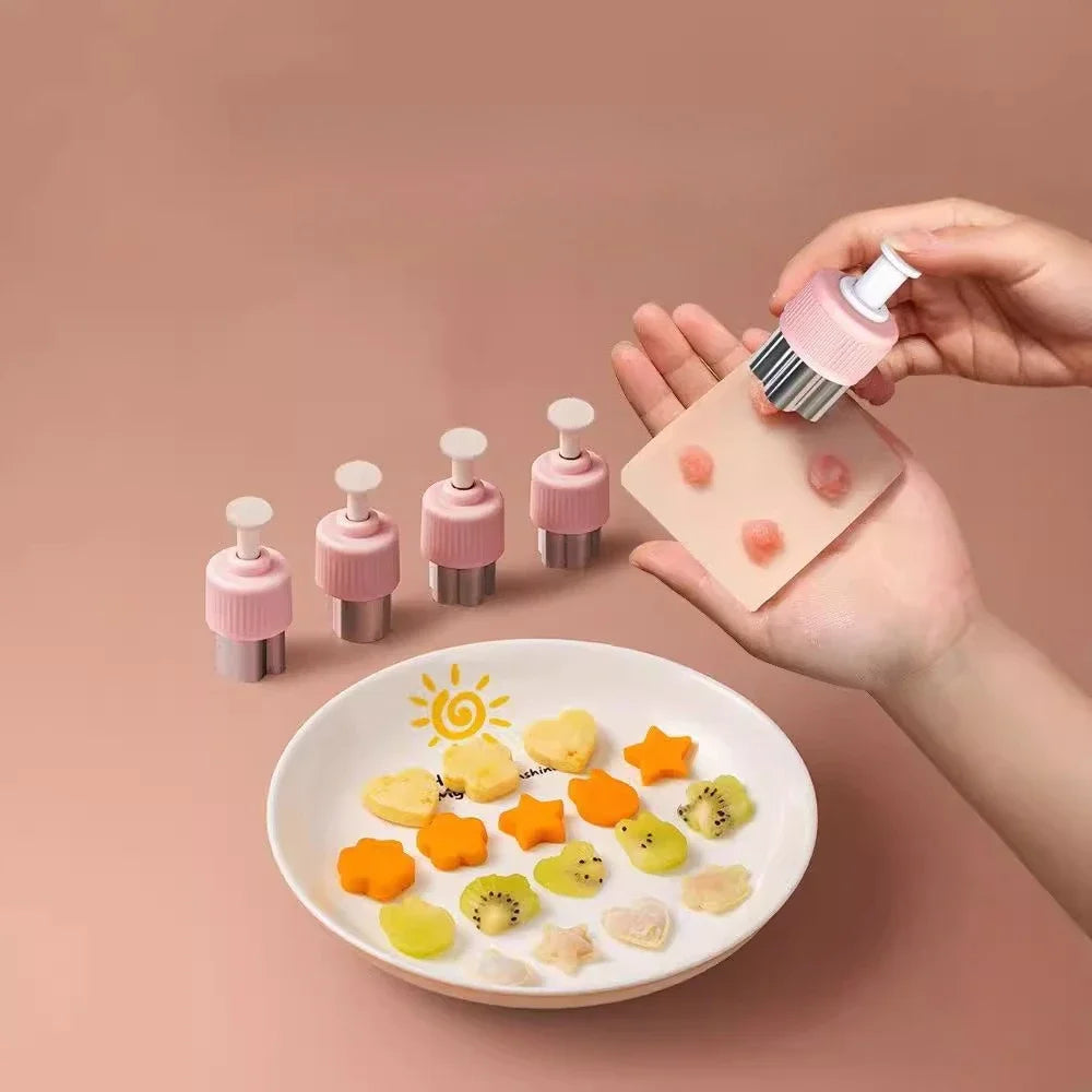 A hand holds a pink silicone mold set for pressing fruit and vegetable shapes onto a white plate.