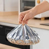 A hand is holding a clear aluminum foil food cover over a cooking appliance.