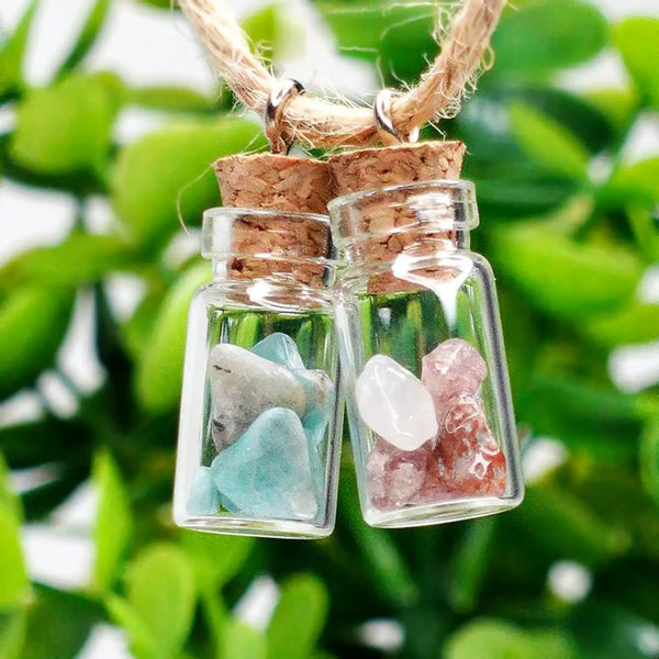 Zwei klare Glasfläschchen mit hellblauen und rosa Quarzkristallen, aufgehängt an einem Naturfasernachse