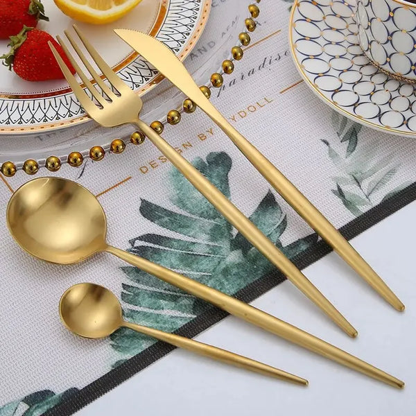 Set aus mattgoldenem Edelstahlbesteck (Gabel, Löffel, Messer) auf gemusterter Serviette.