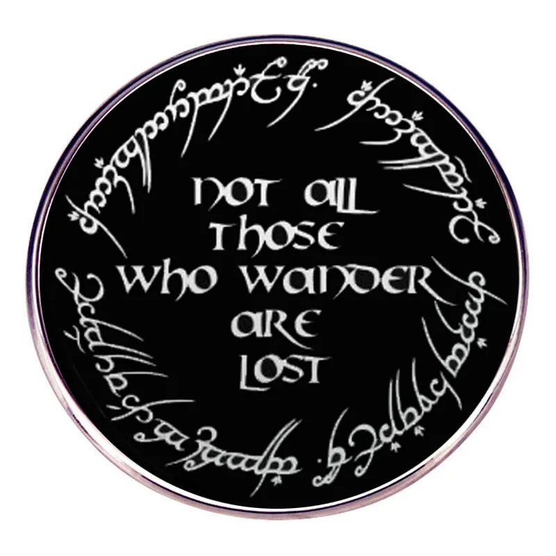 A round black enamel pin featuring white script text that reads Not all those who wander are lost