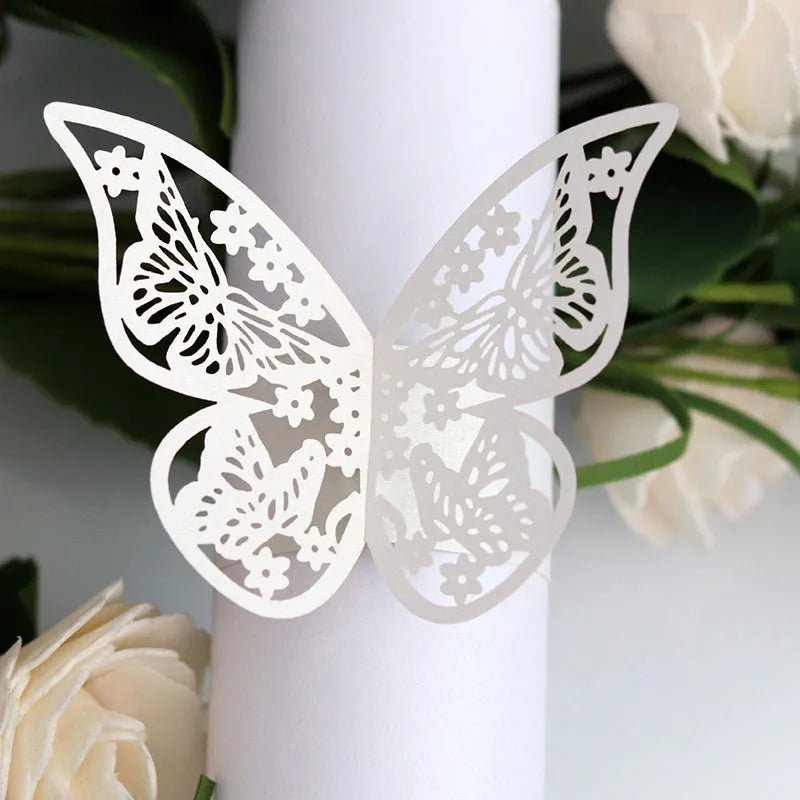 White laser cut butterfly napkin rings displayed against a white cylindrical object and green foliage.
