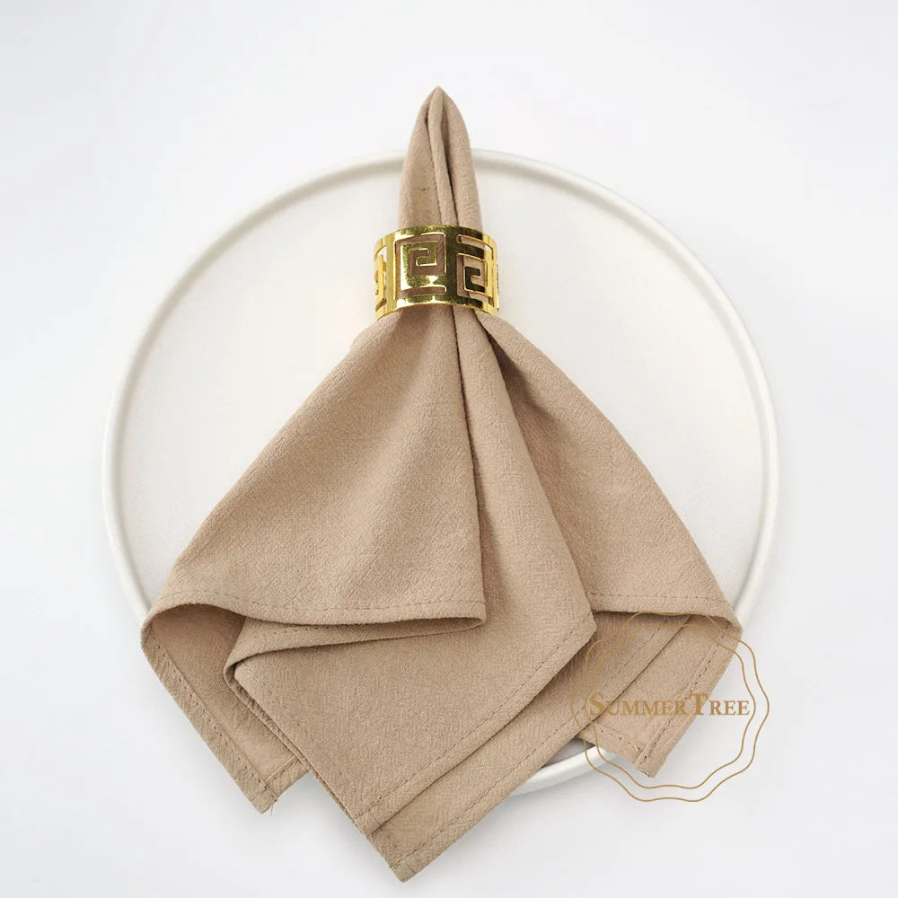A stack of ten beige cotton table napkins tied with a gold patterned ribbon, displayed on a white plate.