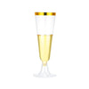 A clear disposable champagne flute with a gold rim and yellow liquid inside.