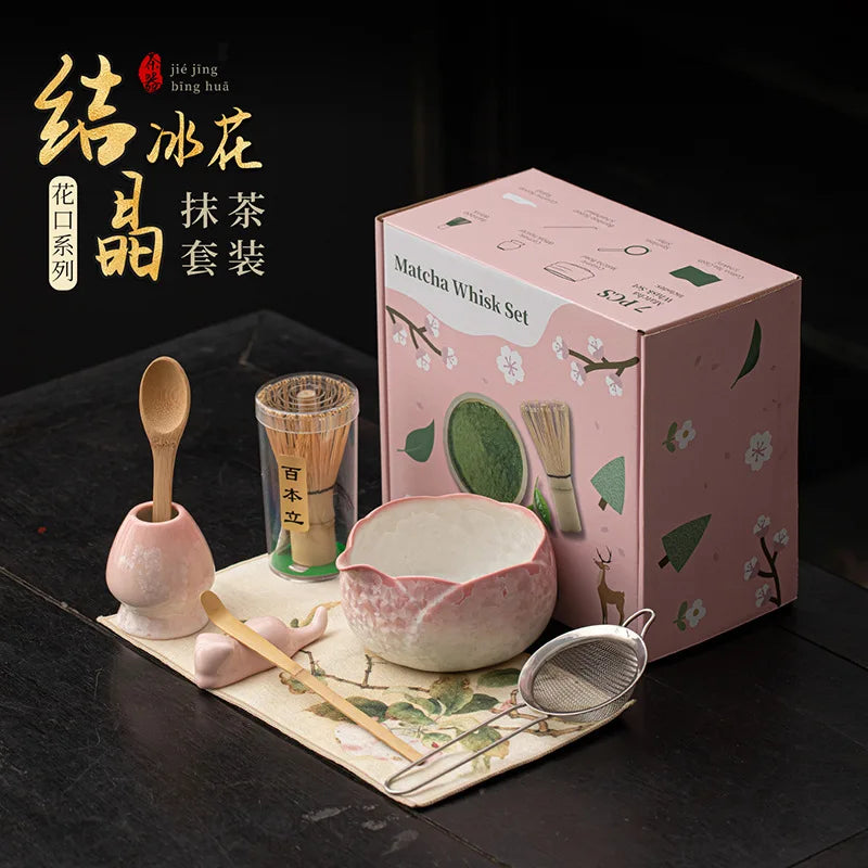 Una caja rosa con un set de batidor de matcha, que incluye un batidor y un cuenco para té, mostrado sobre una superficie oscu