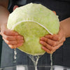 Hands are holding a light green reusable kitchen food filter bag, with liquid dripping from the bottom.