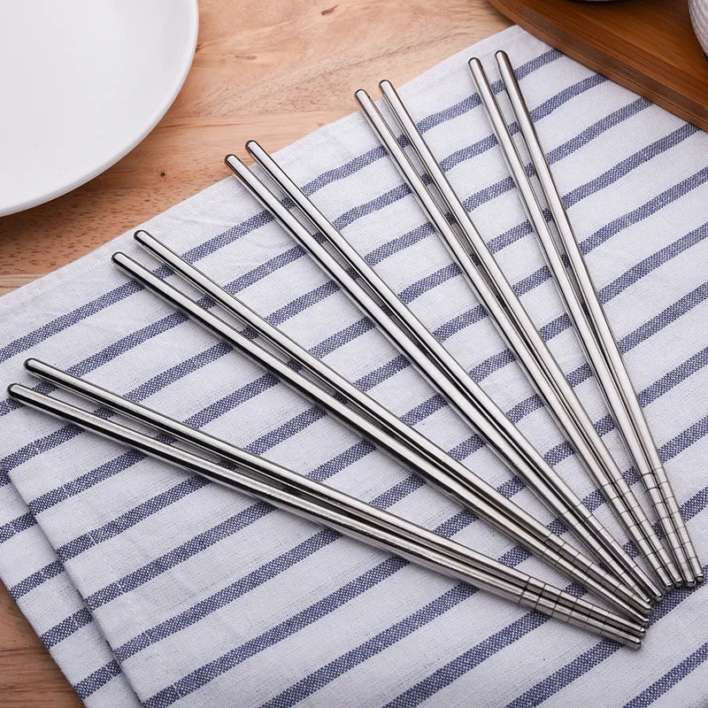 A set of sleek, silver reusable stainless steel chopsticks resting on a striped cloth napkin.