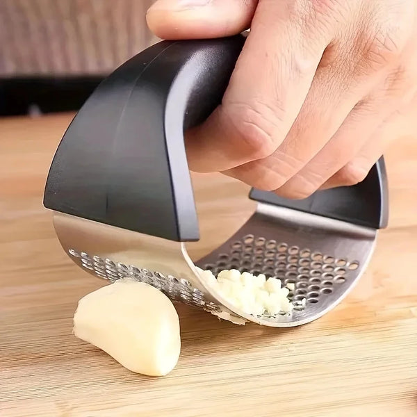 Eine Hand hält eine Edelstahl-Knoblauchpresse und -mörser, mit zerdrückter Knoblauch auf dem Teller.