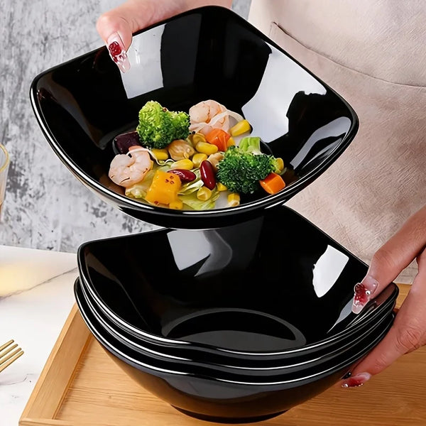 Ein Set von sechs schwarzen Kunststoffschalen zum Kochen wird auf einem Holzbrett präsentiert.