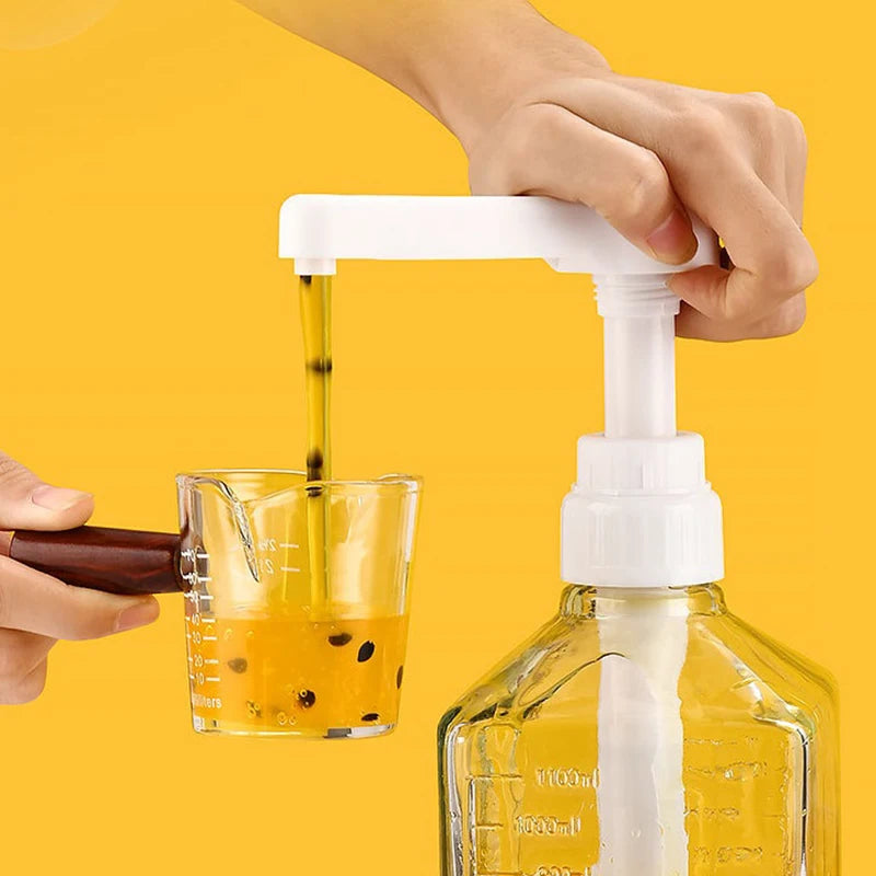 A hand is dispensing syrup from a white pump dispenser into a glass, set against a yellow background.