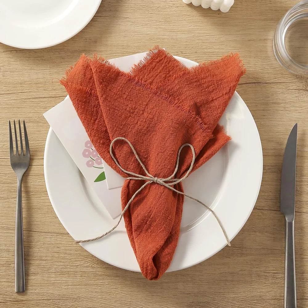 Una pila de servilletas de algodón reutilizables de gasa naranja óxido atadas con cuerda sobre un plato blanco.
