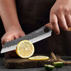 A hand is using a professional stainless steel chef knife to slice a lemon on a dark surface.