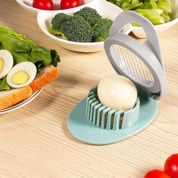 Edelstahl-Eierslicer und Fruchtcutter neben geschnittenen hartgekochten Eiern und Gemüse auf Holzoberfläche.