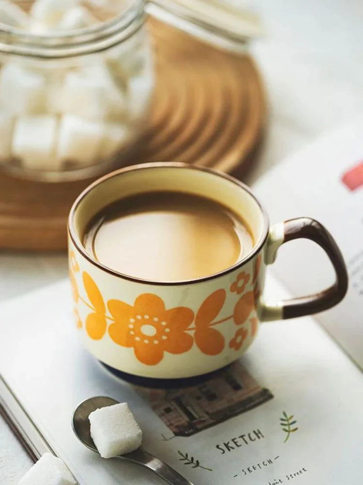 Une tasse à café en céramique avec des motifs floraux orange sur un carnet, à côté d'un petit cube blanc.