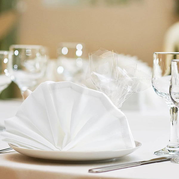 A white plate holds a fan of folded white cloth napkins on a table setting.