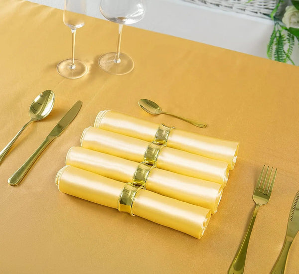 Ein Set Satin-Servietten mit Goldrand auf einem goldenen Tisch mit Besteck und Weingläsern.