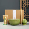 A traditional Japanese matcha tea set featuring a green bowl, bamboo whisk, and wooden utensils displayed in a cardboard box.