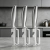 Three stainless steel ergonomic vegetable peelers standing upright on a gray countertop.