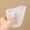 A hand holds a clear silicone measuring cup with red markings, showing various liquid volume measurements.