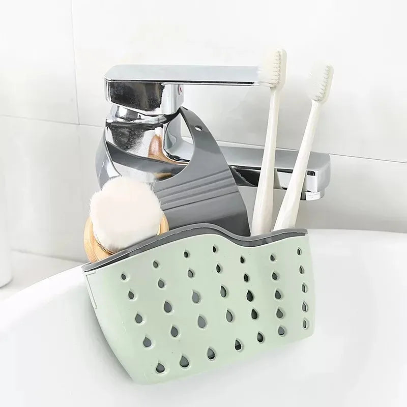 A silver adjustable sink drain hanging sponge rack with white toothbrushes and a light green sponge holder.