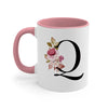 A pink ceramic coffee mug with a black monogram letter Q decorated with floral accents.