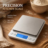 A silver digital kitchen scale with a stainless steel platform is shown on a wooden surface next to flour and a bowl.