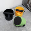 Three coffee grounds containers in black, yellow, and green sitting on a gray surface.